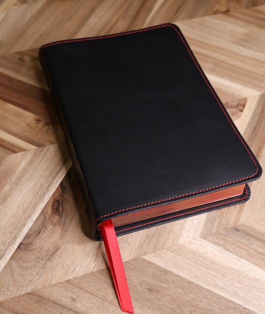 Black leather Bible with a red bookmark on a wooden surface